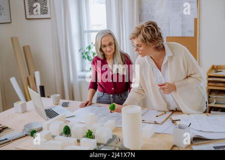 Le donne mature eco architetti con modello di moderni bulidings e progetti che lavorano insieme in ufficio. Foto Stock