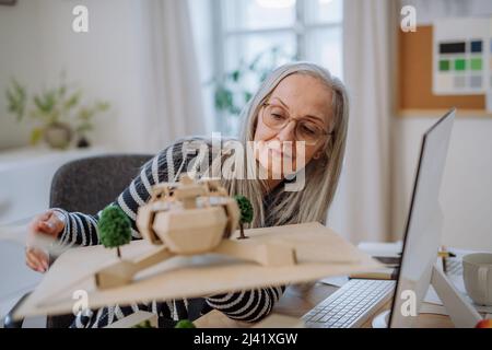 Senior donna architetto che detiene il modello di moderno eco-edificio in ufficio Foto Stock