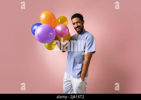 Felice giovane pediatra che tiene palloncini su sfondo rosa Foto Stock