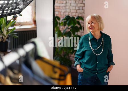 Donna anziana sorridente in posa in elegante showroom. Foto Stock