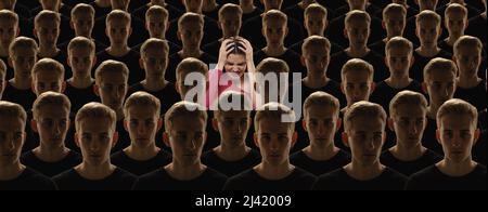 Vista dall'alto della folla grigia di persone identiche con le stesse emozioni e una giovane ragazza diversa, differenza e diversità concetto. Distinguiti dalla folla Foto Stock