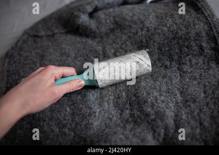 Primo piano mano donna utilizzare il rullo di lanugine sulla giacca di lana rullo di lanugine adesivo tutto in lana appiccicata e capelli persona pulizia abiti di lana con rullo di lanugine Foto Stock