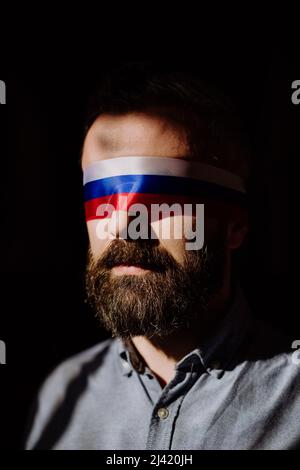 Uomo con bandiera russa cieca su sfondo nero, propaganda russa ha chiuso il concetto degli occhi della gente. Foto Stock