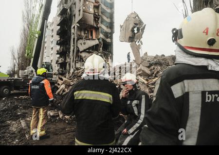 I soccorritori continuano a scavare e rimuovere i detriti da un blocco di appartamenti distrutto che, a quanto pare, seppellì un numero indefinito di civili sotto le macerie. Durante l'accerchiamento russo di Kyiv molti villaggi e sobborghi fuori della città vide feroci combattimenti e brutale occupazione da parte dei russi invasori che hanno causato numerose vittime civili e denunciato crimini di guerra in tutta la regione. Borodyanska, un villaggio di circa 30 miglia fuori da Kiev, ha visto gli attacchi aerei che hanno sepolto un numero sconosciuto di residenti nel seminterrato dei loro edifici di appartamenti. Foto Stock