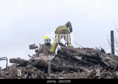 I soccorritori continuano a scavare e rimuovere i detriti da un blocco di appartamenti distrutto che, a quanto pare, seppellì un numero indefinito di civili sotto le macerie. Durante l'accerchiamento russo di Kyiv molti villaggi e sobborghi fuori della città vide feroci combattimenti e brutale occupazione da parte dei russi invasori che hanno causato numerose vittime civili e denunciato crimini di guerra in tutta la regione. Borodyanska, un villaggio di circa 30 miglia fuori da Kiev, ha visto gli attacchi aerei che hanno sepolto un numero sconosciuto di residenti nel seminterrato dei loro edifici di appartamenti. Foto Stock