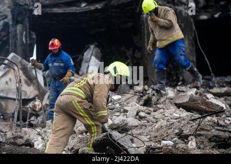 I soccorritori continuano a scavare e rimuovere i detriti da un blocco di appartamenti distrutto che, a quanto pare, seppellì un numero indefinito di civili sotto le macerie. Durante l'accerchiamento russo di Kyiv molti villaggi e sobborghi fuori della città vide feroci combattimenti e brutale occupazione da parte dei russi invasori che hanno causato numerose vittime civili e denunciato crimini di guerra in tutta la regione. Borodyanska, un villaggio di circa 30 miglia fuori da Kiev, ha visto gli attacchi aerei che hanno sepolto un numero sconosciuto di residenti nel seminterrato dei loro edifici di appartamenti. Foto Stock