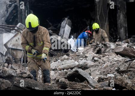 I soccorritori continuano a scavare e rimuovere i detriti da un blocco di appartamenti distrutto che, a quanto pare, seppellì un numero indefinito di civili sotto le macerie. Durante l'accerchiamento russo di Kyiv molti villaggi e sobborghi fuori della città vide feroci combattimenti e brutale occupazione da parte dei russi invasori che hanno causato numerose vittime civili e denunciato crimini di guerra in tutta la regione. Borodyanska, un villaggio di circa 30 miglia fuori da Kiev, ha visto gli attacchi aerei che hanno sepolto un numero sconosciuto di residenti nel seminterrato dei loro edifici di appartamenti. Foto Stock