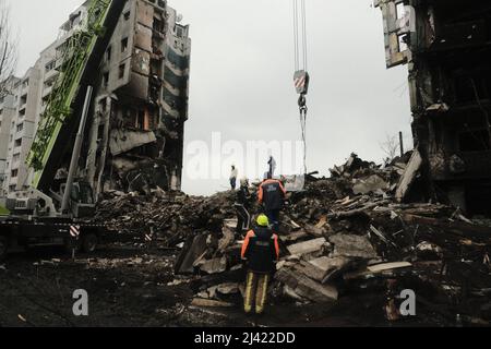 I soccorritori continuano a scavare e rimuovere i detriti da un blocco di appartamenti distrutto che, a quanto pare, seppellì un numero indefinito di civili sotto le macerie. Durante l'accerchiamento russo di Kyiv molti villaggi e sobborghi fuori della città vide feroci combattimenti e brutale occupazione da parte dei russi invasori che hanno causato numerose vittime civili e denunciato crimini di guerra in tutta la regione. Borodyanska, un villaggio di circa 30 miglia fuori da Kiev, ha visto gli attacchi aerei che hanno sepolto un numero sconosciuto di residenti nel seminterrato dei loro edifici di appartamenti. Foto Stock