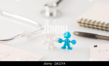 Concetto di assistenza sanitaria familiare, medicina e assicurazione. Figura familiare, cardiogrammi, penna con blocco note e stetoscopio su un banco medico bianco. Lavoro medico Foto Stock