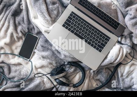 Computer portatile, smartphone e cuffie a letto, vista dall'alto. Foto Stock