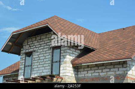 Un primo piano di una mansarda di una casa di un piano e mezzo in costruzione con finestre dormer, tetto in stinco di asfalto, e l'inizio di un balco loft Foto Stock