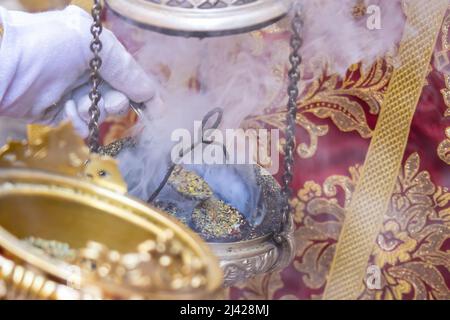 Dettaglio della mano di un ragazzo altare o di un'accolita in una processione della settimana Santa che riempie di incenso uno dei censori Foto Stock