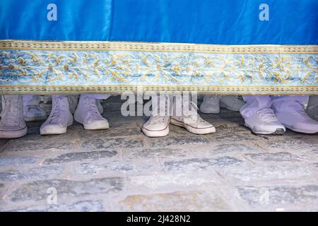 Scarpe bianche dei bearers del costalero sotto la piattaforma della vergine che fa la manovra di svolta lungo una strada della città in una processione di settimana Santa. Questo Foto Stock