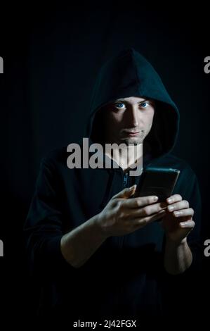 Ritratto di un giovane uomo con cappuccio che usa uno smartphone e guarda la fotocamera come se fosse disturbato Foto Stock