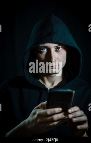 Ritratto di un giovane uomo con cappuccio che usa uno smartphone e guarda la fotocamera come se fosse disturbato Foto Stock