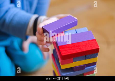 Un bambino gioca un gioco di blocchi di legno colorati jenga, primo piano, fuoco selettivo Foto Stock