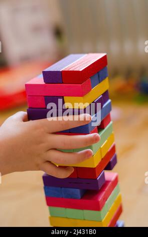 Un bambino gioca un gioco di blocchi di legno colorati jenga, primo piano, fuoco selettivo Foto Stock