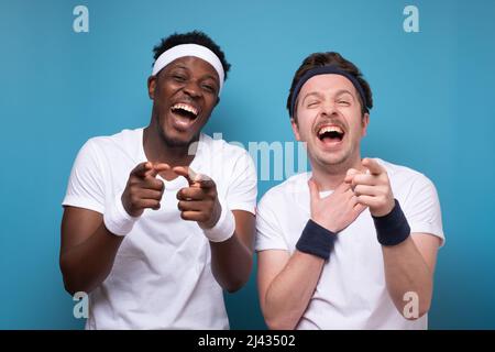 Due giovani uomini allegri che indossano abiti sportivi in piedi isolati su sfondo blu, ridendo Foto Stock