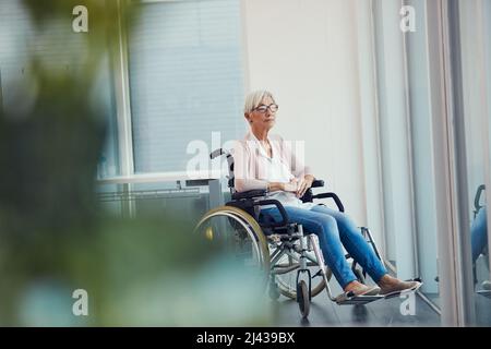 Chi sapeva itd finisce così. Ripresa a tutta lunghezza di una donna anziana che guarda pensierosa mentre si siede sulla sua sedia a rotelle ad una casa di pensionamento. Foto Stock