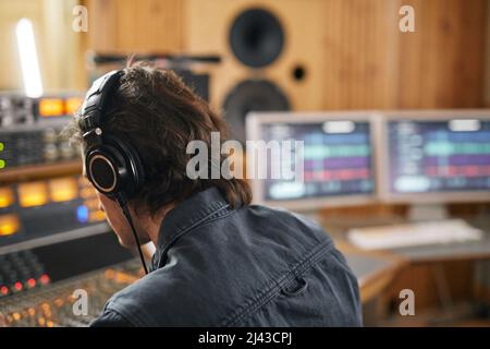 Musicista maschile che indossa le cuffie alla stazione di lavoro audio in studio di registrazione professionale, spazio copia Foto Stock