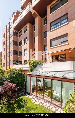 Terrazza coperta con struttura in alluminio marrone e vetro con accesso all'appartamento al piano terra di un condominio residenziale con una ga Foto Stock