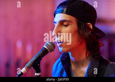 Ritratto del profilo del giovane che canta al microfono in luci colorate da studio, spazio copia Foto Stock