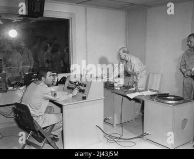 Nella sala di controllo, - il cuore di questa stazione radio, Tech/Sgt. Clifford Johnson, North Hollywood, California, gestisce un controllo del mixer mentre (a destra) Pvt. Eugene T. Twomley, Hollywood, California, guarda fuori la finestra della sala di controllo nello studio principale. Questa nuova stazione è operativa per i membri delle forze Armate in questa zona. E' una stazione da 1.000 watt e si trova a Noumea, Nuova Caledonia. Gennaio 02, 1944. (Foto di Lienhard, U.S. Army Signal Corps). Foto Stock