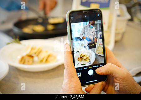 Le mani scattano le foto con il telefono mobile del cuoco in un laboratorio della cucina. Messa a fuoco selettiva sul telefono cellulare in primo piano. Milano, Italia - Marzo 2022 Foto Stock