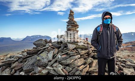 Escursionista maschile in piedi sulla cima di Nuolja, o Njulla, montagna nel Parco Nazionale di Abisko in Svezia artica. Porta Lapponiana, o Lapporten, nella parte posteriore Foto Stock