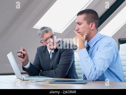 Due uomini d'affari caucasici che discutono sopra un laptop contro l'ufficio in background Foto Stock