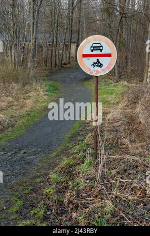 Non ci sono automobili e non ci sono motocicli accanto a un sentiero che conduce a una foresta in una giornata nuvolosa di primavera. Cartello stradale in zona rurale remota. Foto Stock
