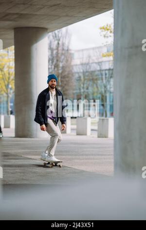 Ritratto del ragazzo skater attivo che si bilancia sullo skateboard su sfondo urbano ha messo a fuoco lo skateboarder che si muove su skate board all'aperto. Foto Stock