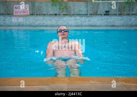 un ragazzo con bicchieri nuota in una grande piscina Foto Stock