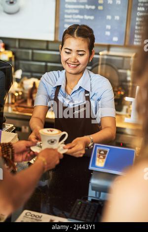 Preparato con cura. Shot di un giovane barista felice che lavora dietro il registratore di cassa in un bar. Foto Stock