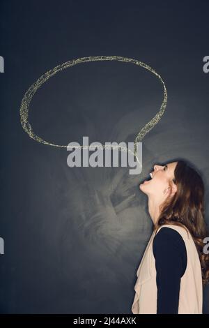 Non tenere indietro. Studio girato di una giovane donna in posa con un gesso illustrazione di una bolla di discorso su uno sfondo scuro. Foto Stock