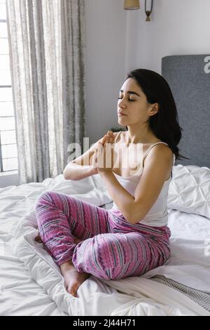 Giovane donna latina meditating usando le cuffie sul letto a casa in Messico America Latina Foto Stock