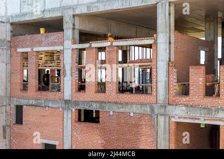muratura delle pareti esterne di una struttura monolitica a telaio, formazione di aperture per finestre con posa di travi in calcestruzzo, fuoco selettivo Foto Stock