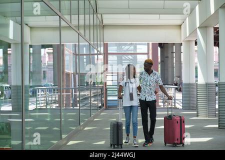 Giovani passeggeri neri con valigie che camminano lungo la strada vicino all'aeroporto. Foto Stock