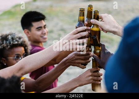 Gruppo di amici multirazziali tostatura con bottiglie di birra Foto Stock