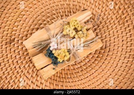 Vista dall'alto su bastoncini di palo santo con mazzi di fiori secchi su sfondo di paglia naturale. Bastoni di legno Santo per la meditazione e le pratiche spirituali. ESO Foto Stock