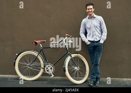 Perché non godere la vita viaggio verso il verde. Ritratto di un giovane che posava con la bicicletta contro un muro scuro. Foto Stock