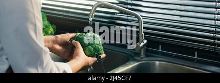 Asian mani donna lavaggio verdure broccoli e preparazione cibo sano in cucina. Foto Stock