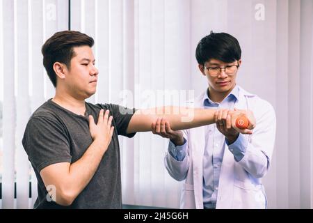 Asian giovane fisioterapista maschile aiutando il paziente con sollevamento manubri esercizi in clinica. Foto Stock