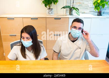 Due addetti al ricevimento indossano una maschera facciale mentre lavorano al banco ricevimento di un centro di fisioterapia. Foto Stock