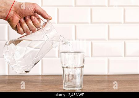 Una mano dell'uomo che versa l'acqua pura fresca dalla bottiglia in un bicchiere sul tavolo, concetto di salute e dieta Foto Stock