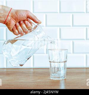 Una mano dell'uomo che versa l'acqua pura fresca dalla bottiglia in un bicchiere sul tavolo, concetto di salute e dieta Foto Stock