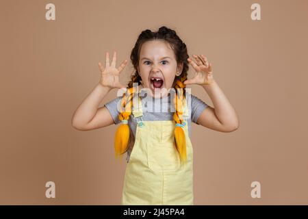 Ritratto di bambina giocosa con pigtail giallo kanekalon, fingendo di essere spaventoso con le mani e bocca aperta indossando tuta gialla Foto Stock
