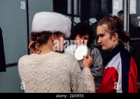 Una giovane donna prova su un cappello bianco con gli amici in un mercato delle pulci a Mosca, Russia, maggio 1990. Foto Stock