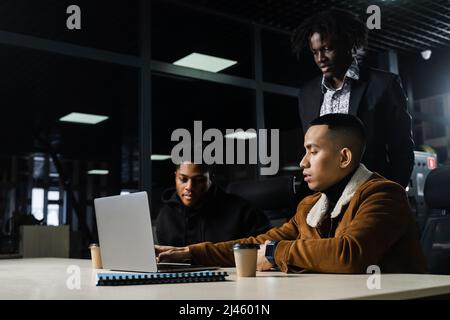 Lavoro di squadra online con il notebook. Colleghi africani neri e asiatici. 3 uomini d'affari multietnici guardano una videoconferenza con colleghi e datori di lavoro Foto Stock