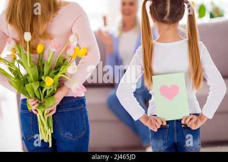 Ritratto di tre persone nascondersi dietro la schiena carta fiori freschi complimentandosi casa al chiuso Foto Stock